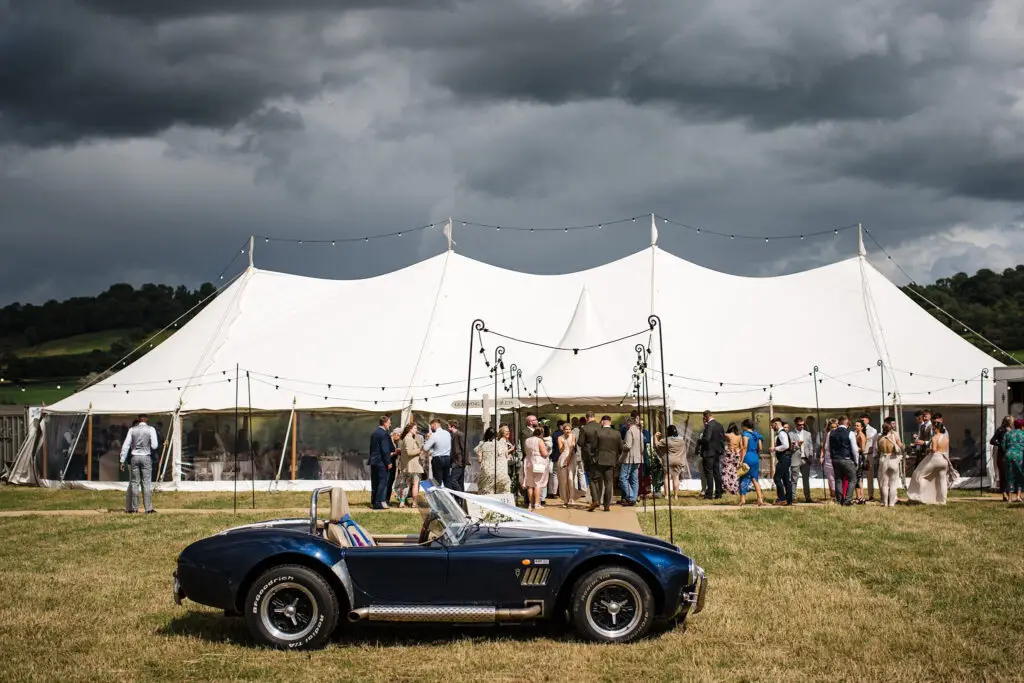 Classic blue convertible parked in front of a luxury wedding marquee in Gloucestershire