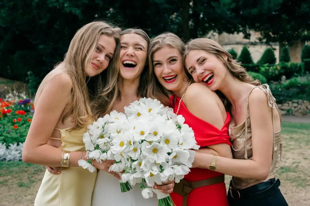 Bride laughing with bridesmaids holding white daisy bouquets in Bath
