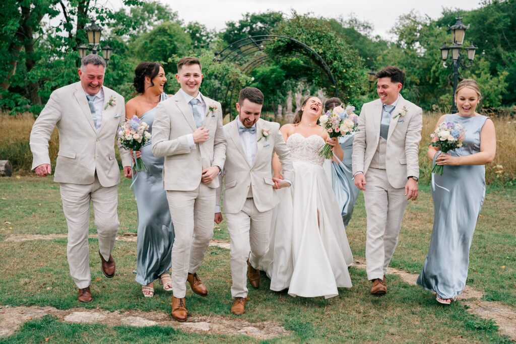 Bridal party laughing and walking through the gardens at Berwick Lodge