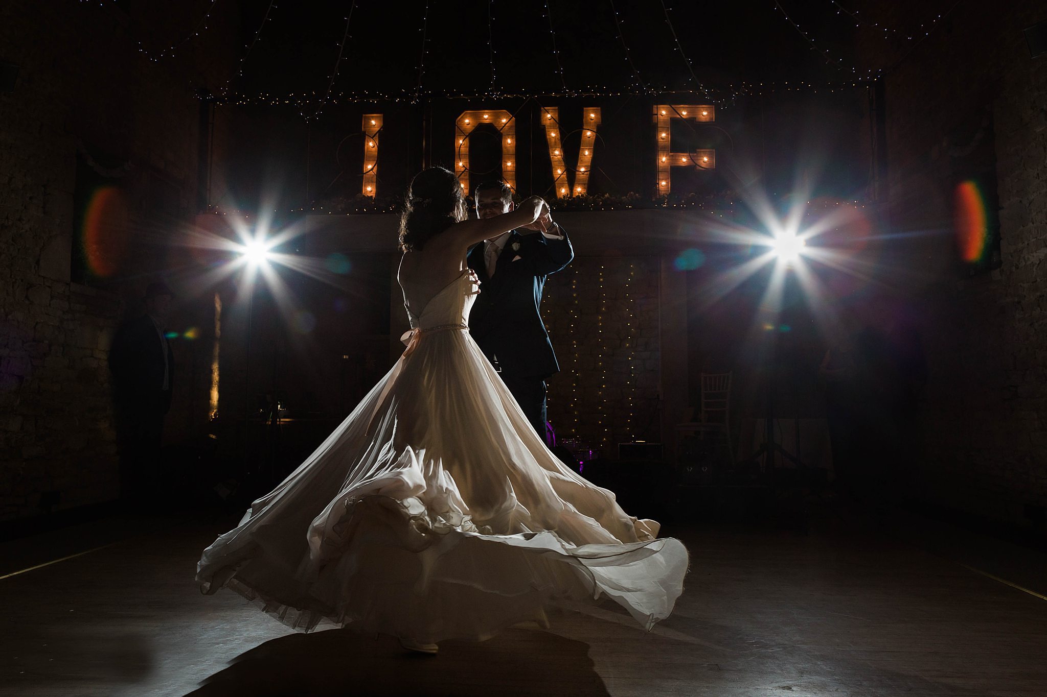 Bride and groom share their first dance under fairy lights in a rustic barn.