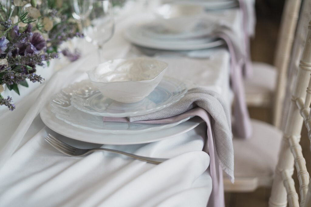Elegant table setting with white plates, lilac napkins, and soft linen at Elmore Court wedding.